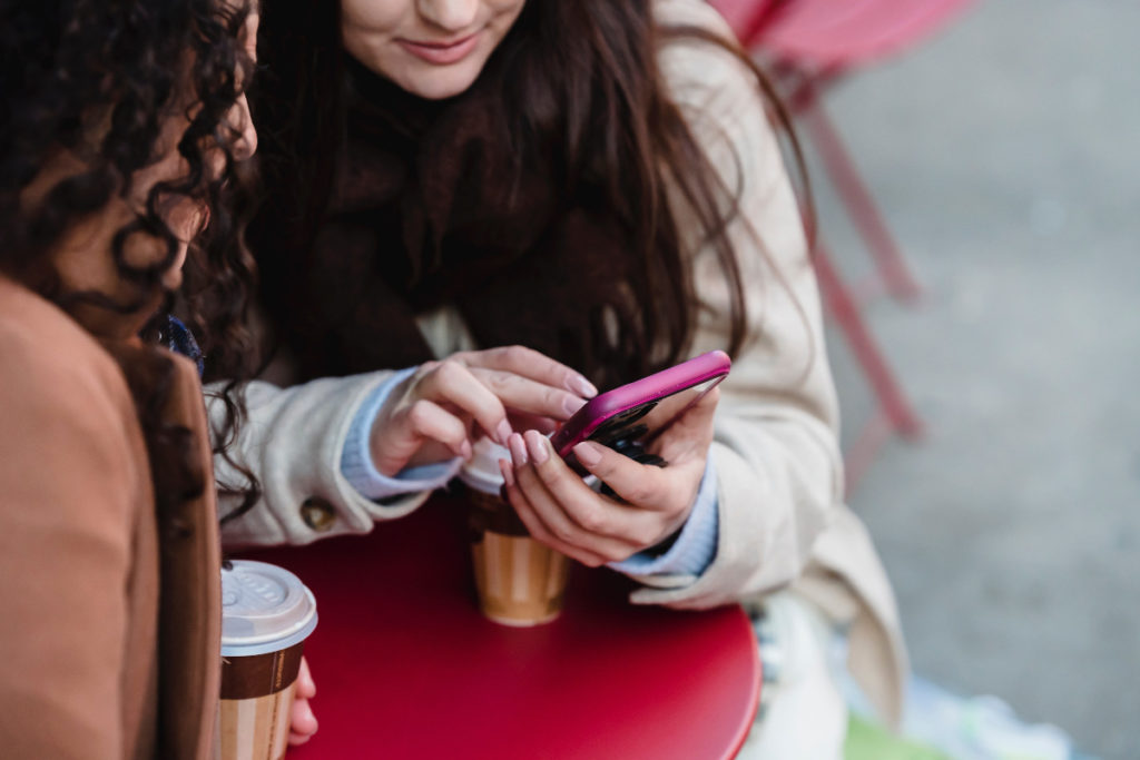Zwei Frauen schauen gemeinsam auf ein rosafarbenes Smartphone.